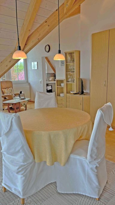 Heller Essbereich mit rundem Tisch, Stühlen und offenen Regalen im Hintergrund.