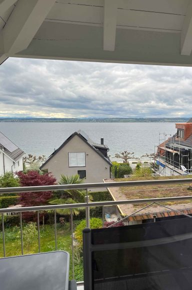 Blick auf einen See mit Häusern und bewölktem Himmel im Hintergrund.