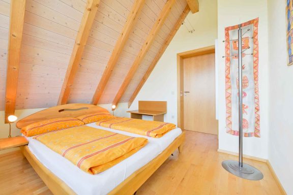 Helles Schlafzimmer mit einem Doppelbett, Holzdecken und einem Stehlampe in der Ecke.